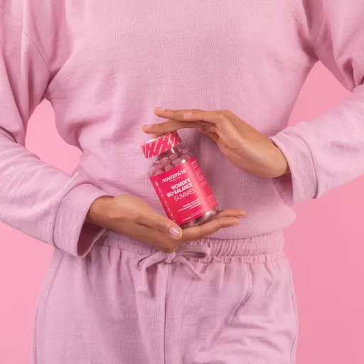 Lady dressed in pink holding a bottle of Novomins Women's Bio-Balance Gummies