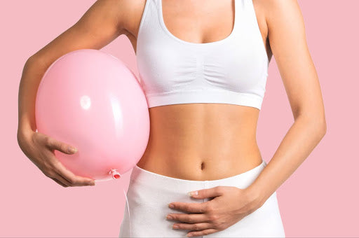 Women holding pink balloon whilst holding stomach in physical discomfort because of bloating